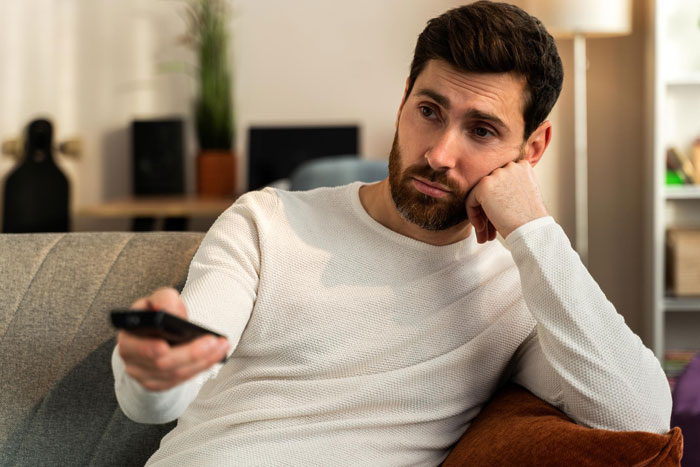 Man looking unmotivated on couch holding remote control, reflecting ungrateful husband and support parenting challenges. Man looking unmotivated on couch holding remote control, reflecting ungrateful husband and support parenting challenges.