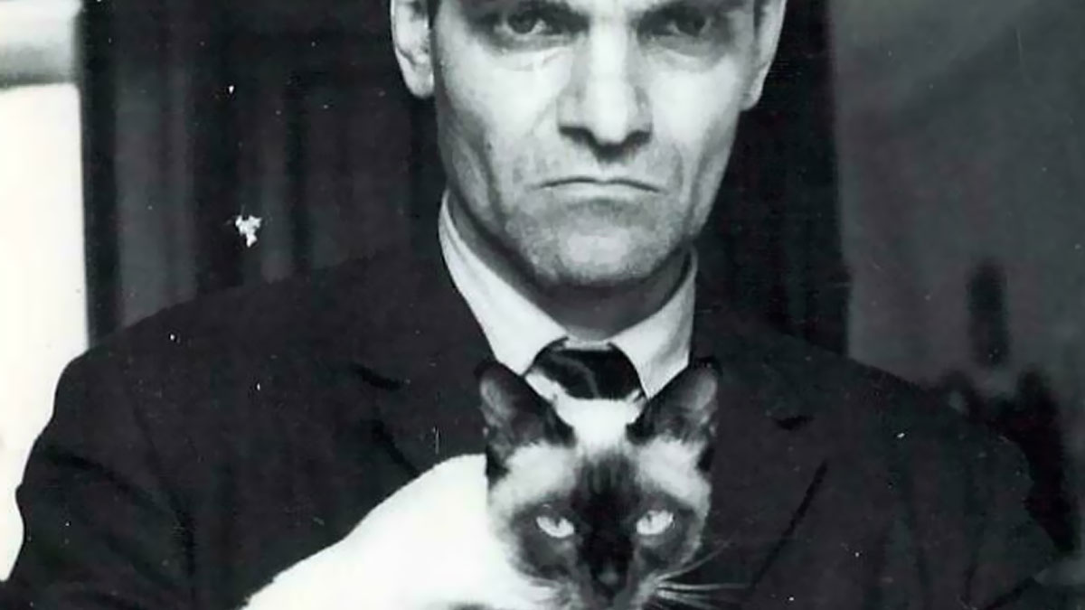Black and white historical photo of a serious man holding a Siamese cat, illustrating unique historical photos with deep backstory.