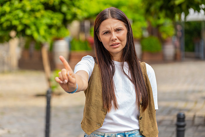 Young woman with long hair wearing a vest and white t-shirt making a stop gesture while walking outdoors. Young woman with long hair wearing a vest and white t-shirt making a stop gesture while walking outdoors.