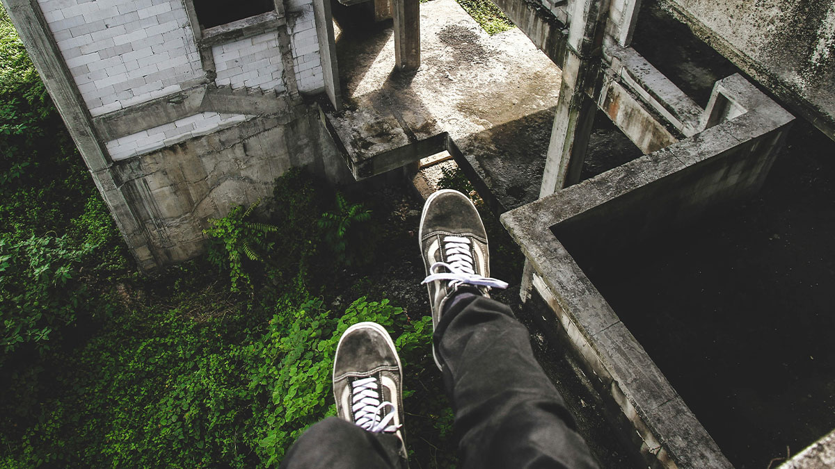 View from an urban exploreru2019s perspective looking down at abandoned concrete structures and overgrown greenery below.