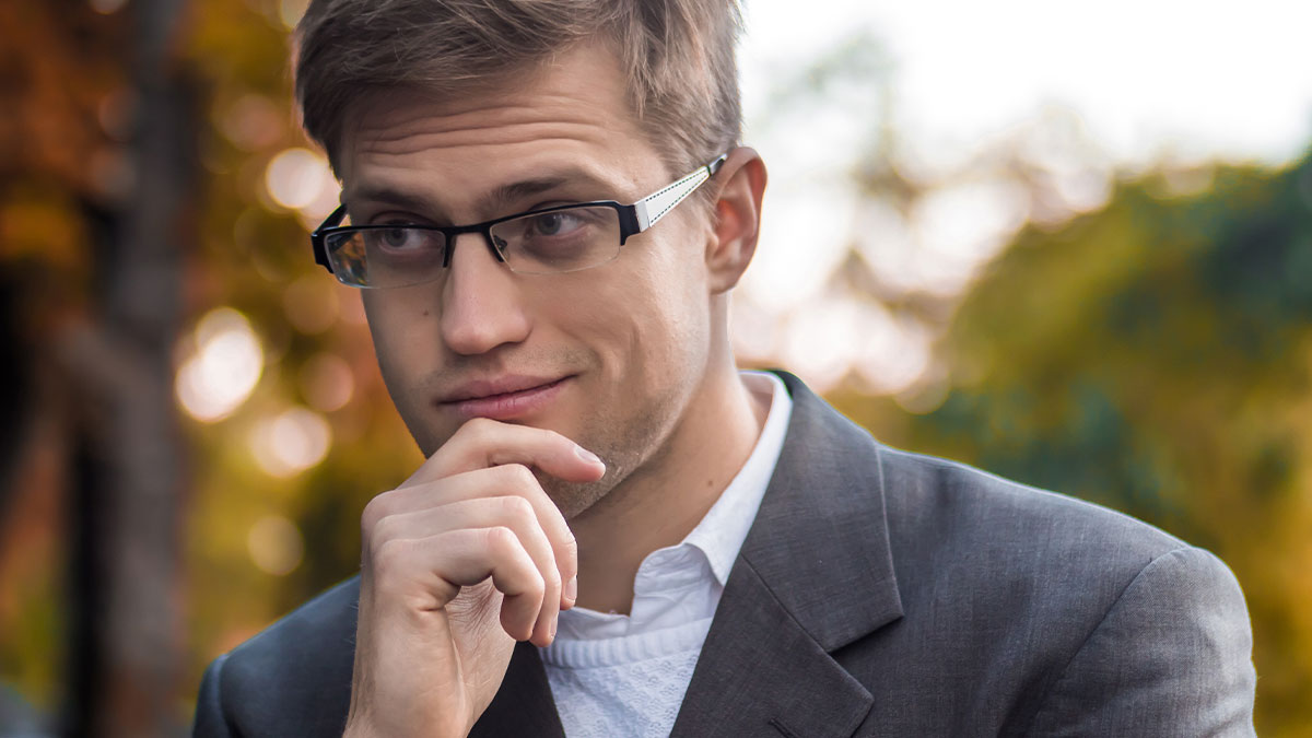 Thoughtful man wearing glasses and a suit, considering a perfect loophole after boss forbids time off at work.