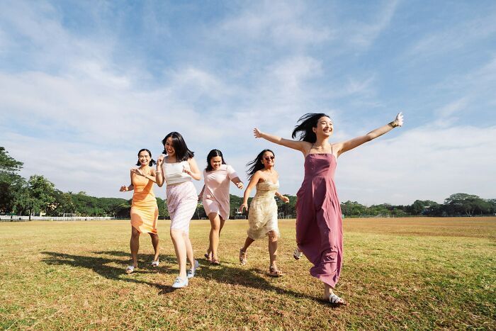 A group of joyful women walking and laughing in a sunny open field, representing positive stereotypes about various countries.