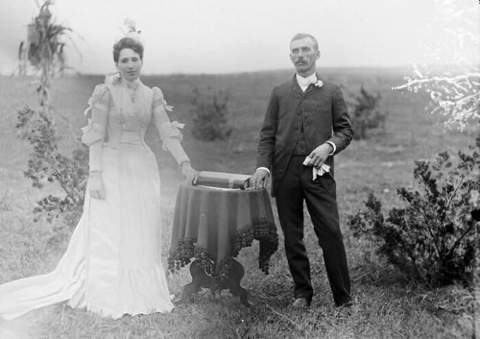 Victorian-Edwardian pictures of a man and woman outdoors in period attire standing by a small table with a lace cloth.