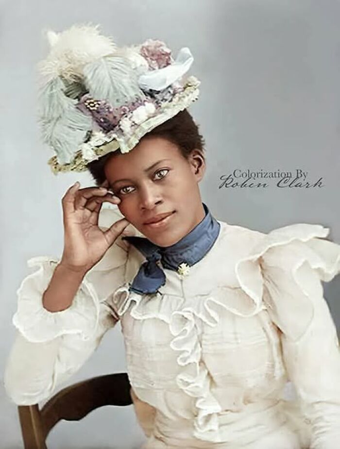 Victorian-Edwardian pictures of a woman in a ruffled dress and ornate hat, colorized portrait with a soft gray background.