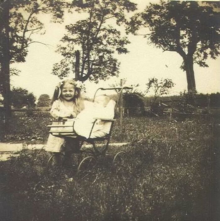 Young girl smiling outdoors with a vintage pram and baby in a field, Victorian Edwardian pictures style.