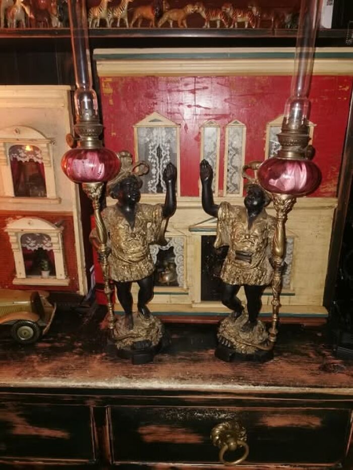 Pair of Victorian-Edwardian pictures featuring antique lamps with ornate figurines on a wooden vintage cabinet surface.
