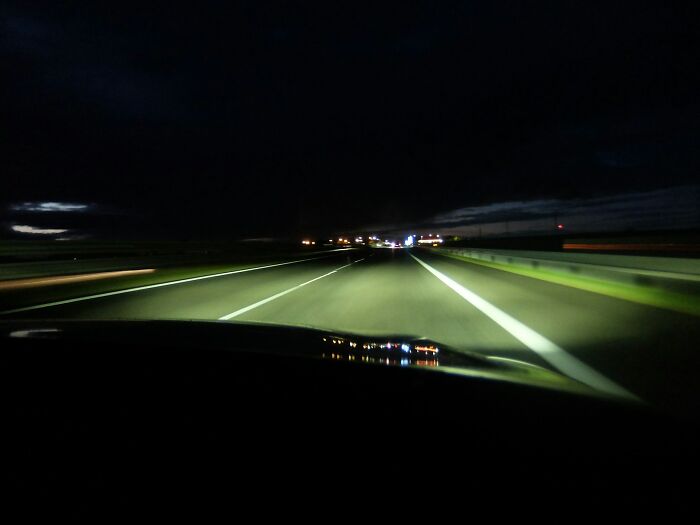 Dark highway at night seen through a car windshield, capturing eerie and unsettling surveillance camera footage.