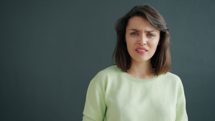 Young woman in a green sweater looking confused, relating to confronting a family over watermark removal on photos.
