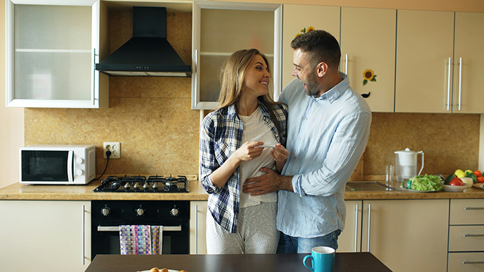 Woman smiling and talking with man in kitchen, asking about stepchildren and home or boarding school options. Woman smiling and talking with man in kitchen, asking about stepchildren and home or boarding school options.