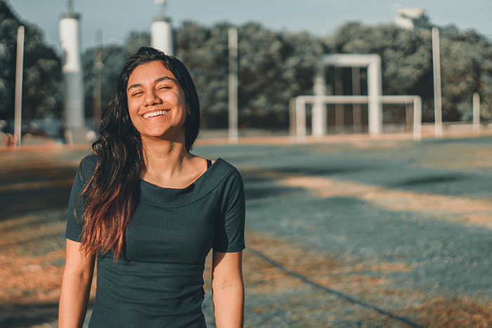 Young woman smiling outdoors on a sunny day, representing an avid walker doing 20K steps per day. Young woman smiling outdoors on a sunny day, representing an avid walker doing 20K steps per day.