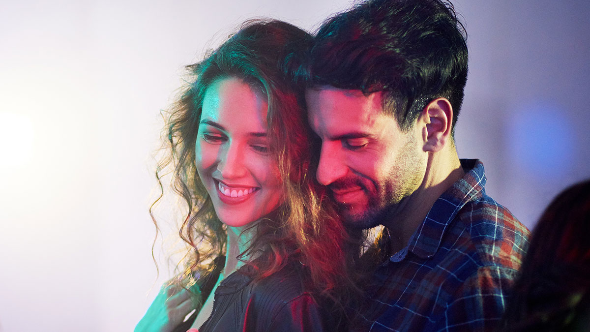 A smiling couple enjoying a close moment with colorful lighting, illustrating men and women relationship dynamics.