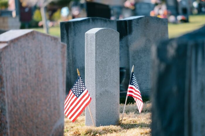 Gravestones in a cemetery with American flags, illustrating themes related to cancer and hard times.