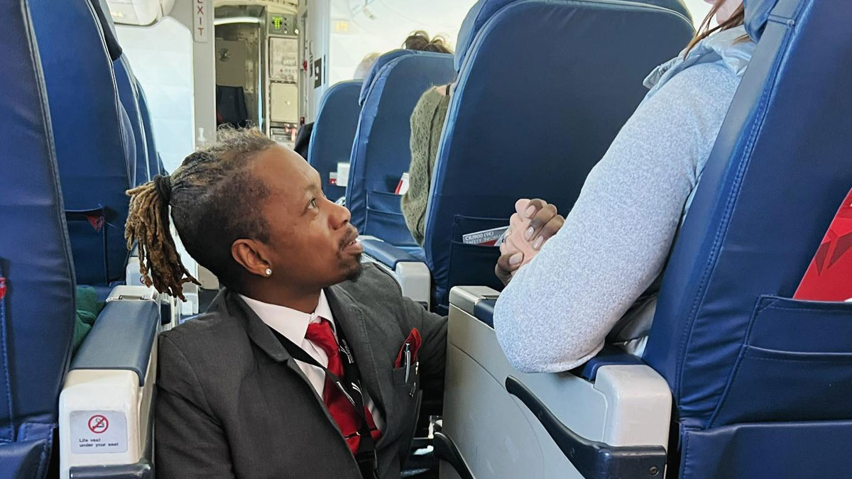 Man in suit with red tie kneeling in airplane aisle, making total strangers day and restoring faith in humanity.