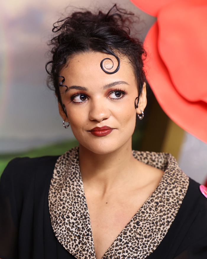 Actress with curled hair and leopard print collar reacting to Wicked cast selfie controversy on disability inclusion. Actress with curled hair and leopard print collar reacting to Wicked cast selfie controversy on disability inclusion.