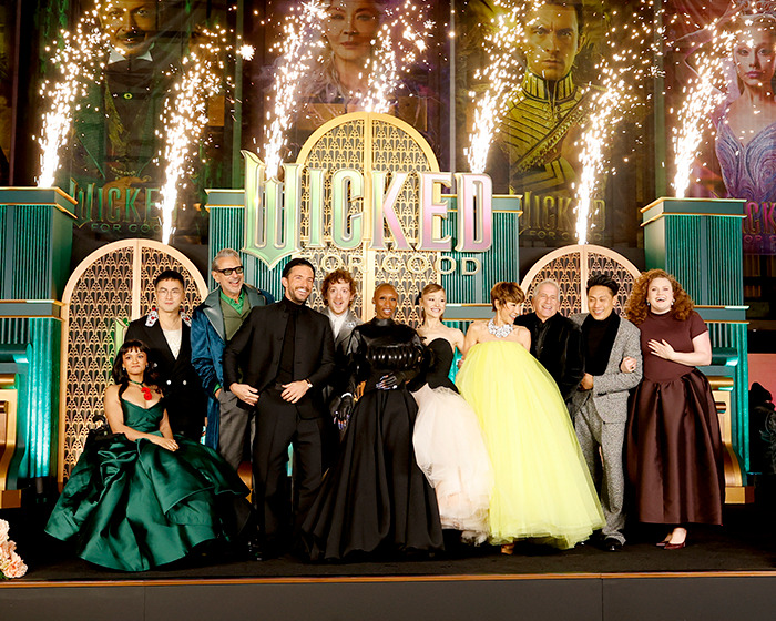 Wicked cast posing on stage with fireworks during event, sparking debate on disability inclusion and exclusion issues. Wicked cast posing on stage with fireworks during event, sparking debate on disability inclusion and exclusion issues.