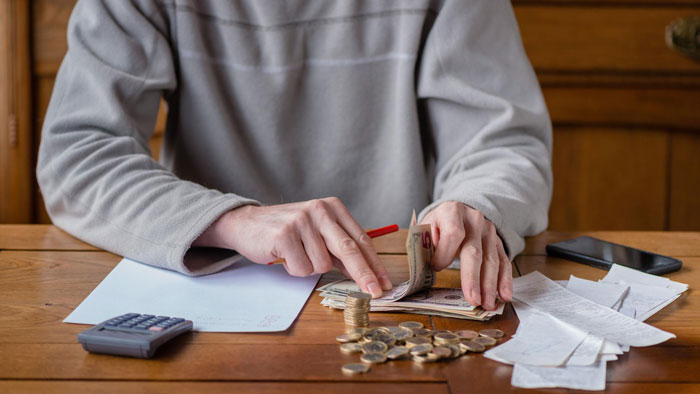 Man counting money and coins at a table with receipts and a calculator, illustrating financial support for in-laws. Man counting money and coins at a table with receipts and a calculator, illustrating financial support for in-laws.