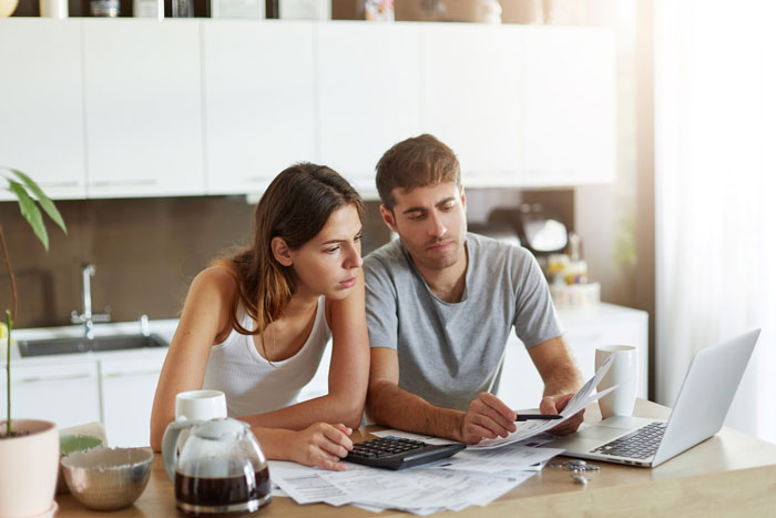 Couple reviewing bills and financial documents at kitchen table, stressed about in-laws and family support issues. Couple reviewing bills and financial documents at kitchen table, stressed about in-laws and family support issues.