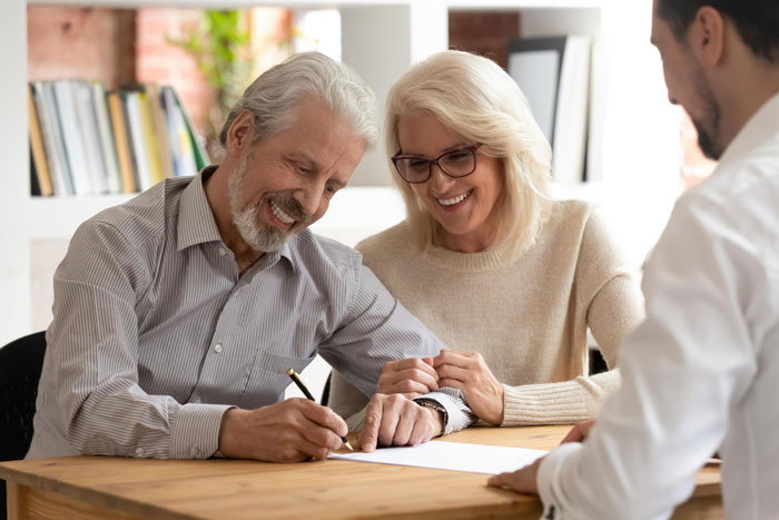 Older couple smiling and signing documents with a professional, illustrating man supporting his in-laws and will issues.