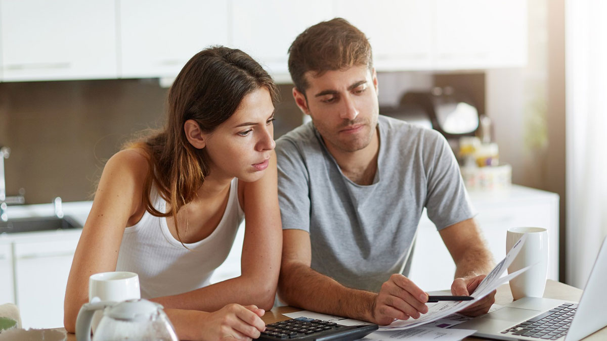 Couple reviewing bills and documents at kitchen table, concerned about man houses and supports his in-laws financial situation.