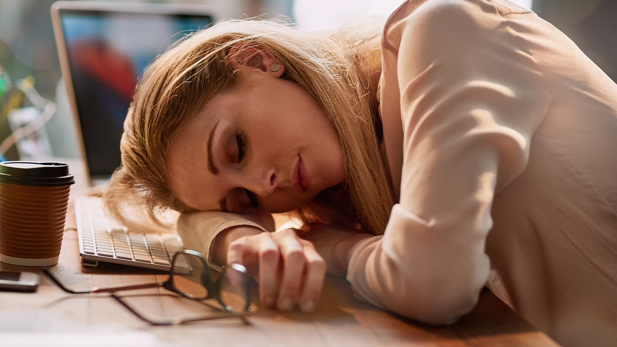 Tired woman resting head on desk with keyboard and coffee cup, representing man treats wife like servant theme.