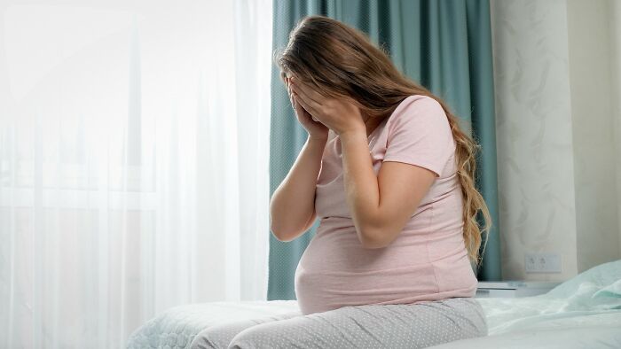 Pregnant woman sitting on bed with face in hands, representing emotional pain and insensitive cancer comments.