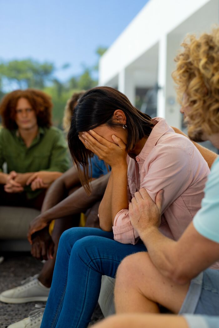 Young woman covering face in distress while others offer support during a group discussing insensitive things said to people with cancer.