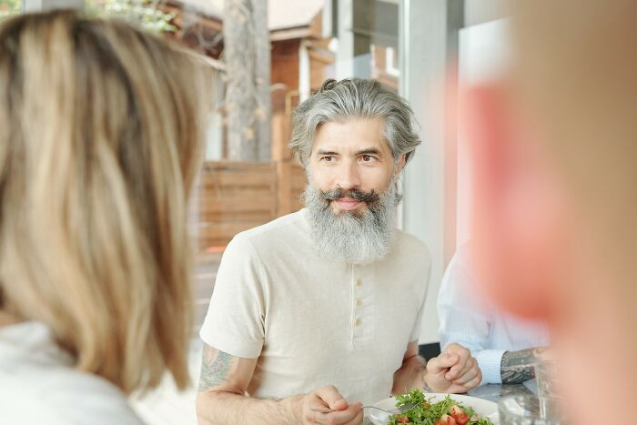 Middle-aged man with gray beard talking to a woman, representing insensitive things said to people having a hard time.
