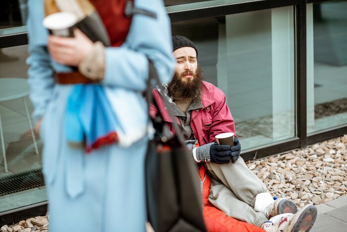 Man sitting on the ground with a coffee cup, appearing distressed, highlighting insensitive things said to people struggling.