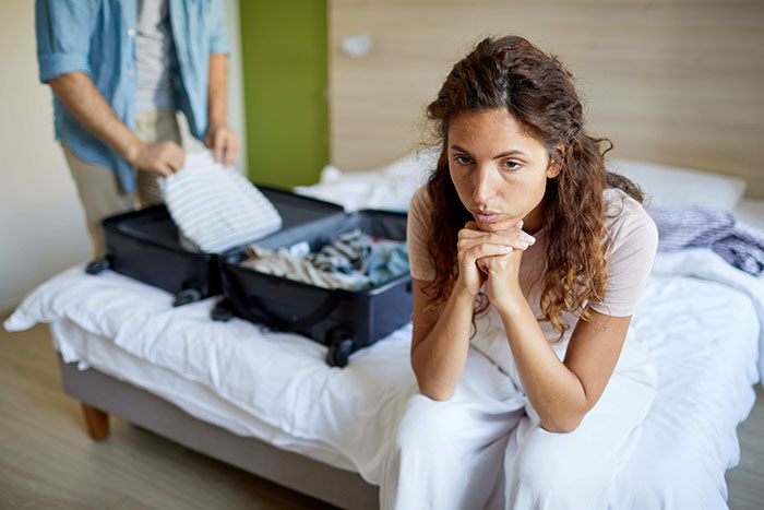 Woman looks worried as man packs suitcase for suspicious work trip, triggering relationship doubts and tension in the room. Woman looks worried as man packs suitcase for suspicious work trip, triggering relationship doubts and tension in the room.