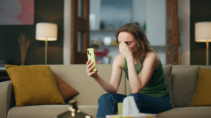 Woman sitting on couch looking distressed while holding phone, reflecting on suspicious work trip and relationship doubts. Woman sitting on couch looking distressed while holding phone, reflecting on suspicious work trip and relationship doubts.