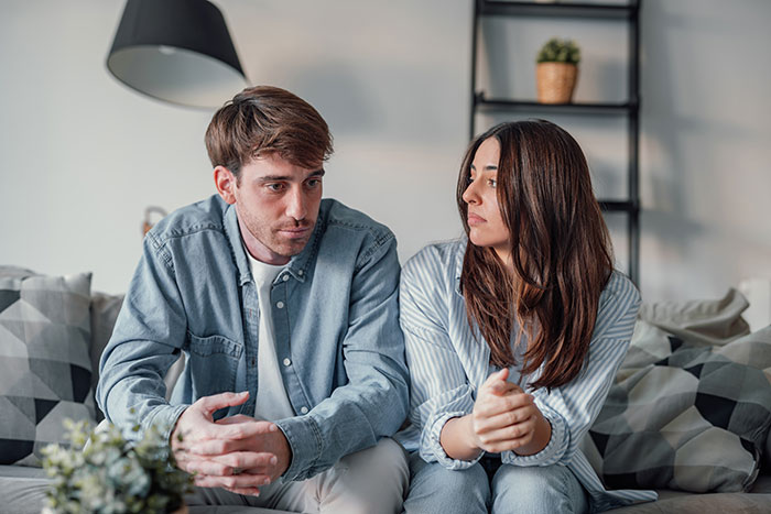 Young couple sitting on couch looking upset, depicting tension over guy secretly giving his sister a key to GF’s house.