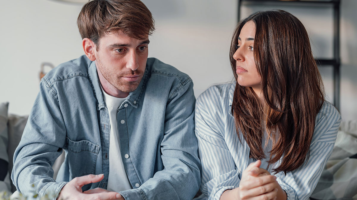 Couple sitting on couch with tense expressions, depicting conflict over secretly giving sister a key to girlfriendu2019s house.