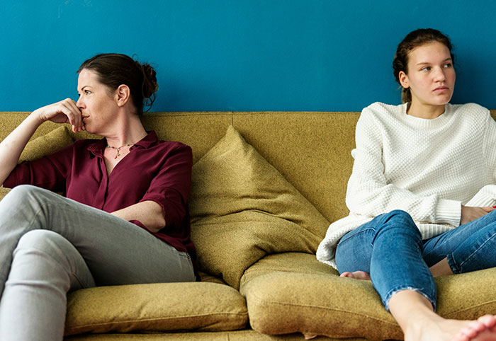 Two women sitting apart on a couch looking upset, illustrating emotional distance and woman child behavior.