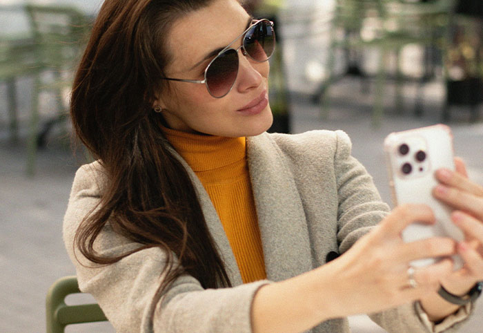 Woman child taking a selfie outdoors wearing sunglasses and a beige coat with a mustard turtleneck sweater