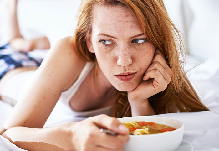 Young woman child lying on bed with bowl of soup, looking thoughtfully to the side in a relaxed setting