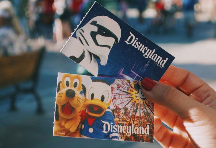 Hand holding colorful Disneyland tickets featuring popular characters Pluto and Donald Duck, symbolizing woman child interests.