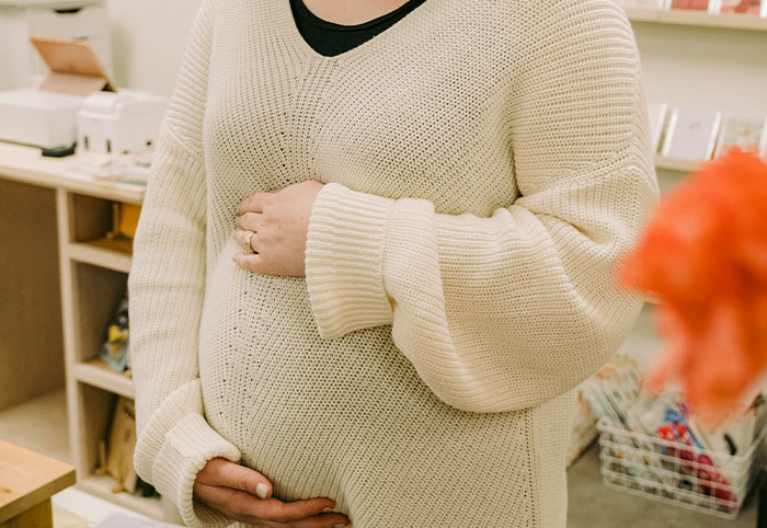 Pregnant woman in a cozy cream sweater holding her belly indoors, reflecting themes of woman child growth and care.