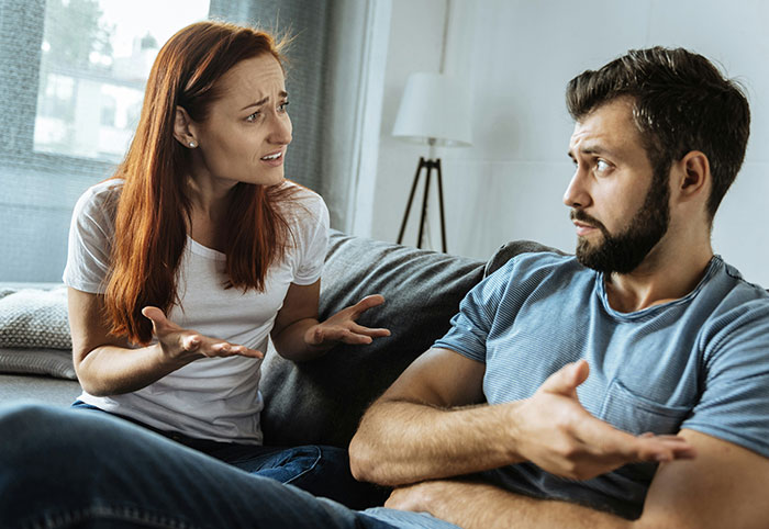 A woman expressing frustration while a man listens, illustrating behaviors of a woman child in a tense moment on the couch.