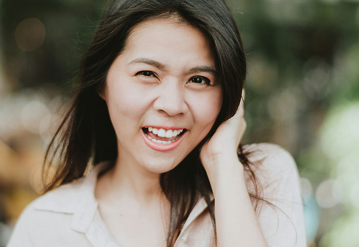 Smiling young woman touching her hair outdoors, expressing confident and playful woman child attitude in natural light.