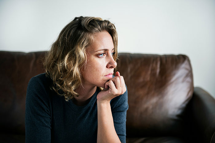 Woman with curly blonde hair sitting on a brown couch, looking thoughtful and upset about favorite grandchild snubs. Woman with curly blonde hair sitting on a brown couch, looking thoughtful and upset about favorite grandchild snubs.
