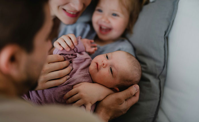 Mother and father holding a newborn baby while toddler smiles, highlighting favorite grandchild and family tension. Mother and father holding a newborn baby while toddler smiles, highlighting favorite grandchild and family tension.