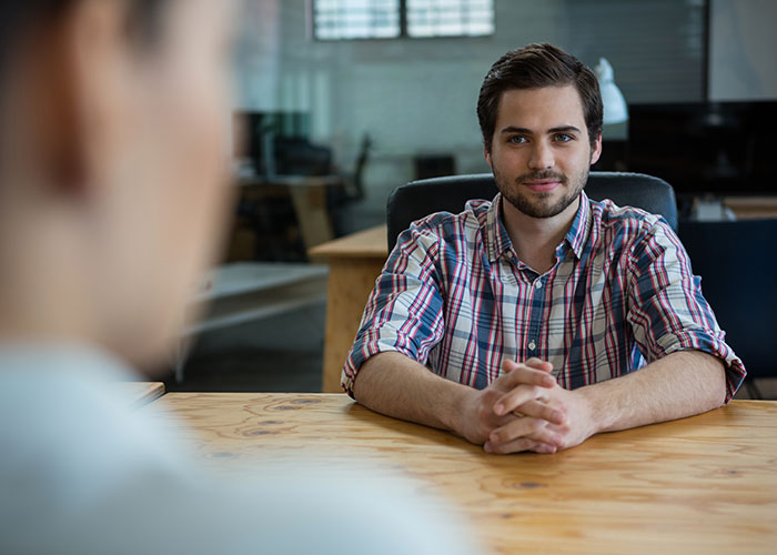 Young man in a plaid shirt sitting at a table, symbolizing a jobless partner in a relationship discussion. Young man in a plaid shirt sitting at a table, symbolizing a jobless partner in a relationship discussion.