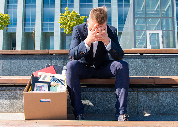 Man in suit sitting on steps with head in hands next to box of personal items after job loss or breakup. Man in suit sitting on steps with head in hands next to box of personal items after job loss or breakup.