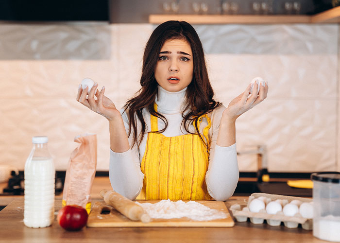 Woman in a yellow apron hesitant to cook a foreign traditional Christmas spread in a modern kitchen setting. Woman in a yellow apron hesitant to cook a foreign traditional Christmas spread in a modern kitchen setting.
