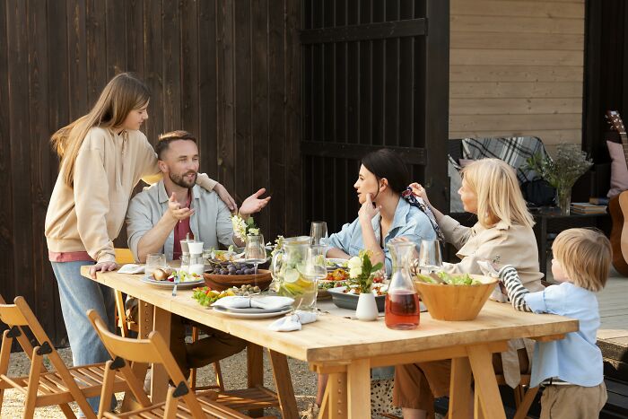 Family enjoying a lively outdoor meal prepared by wife, showcasing feast and fun with loved ones gathered around the table. Family enjoying a lively outdoor meal prepared by wife, showcasing feast and fun with loved ones gathered around the table.