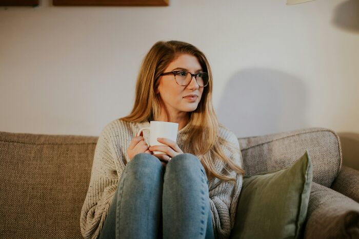 Woman sitting on a couch holding a mug, looking worried and thoughtful, depicting a lonely widower company scenario. Woman sitting on a couch holding a mug, looking worried and thoughtful, depicting a lonely widower company scenario.