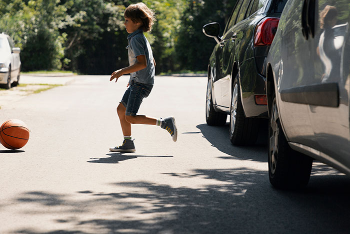 Child running into traffic between parked cars on a sunny street, highlighting the danger of kids running into traffic. Child running into traffic between parked cars on a sunny street, highlighting the danger of kids running into traffic.