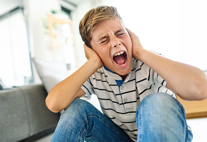 Teen boy covering ears and screaming, experiencing distress after being yelled at for not stopping younger kid running into traffic.