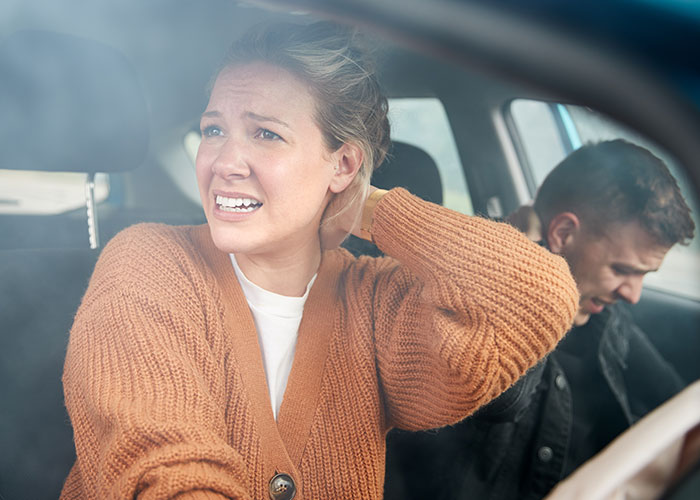 Upset couple inside a car after crash, woman wearing brown sweater showing distress, man in black jacket seated behind. Upset couple inside a car after crash, woman wearing brown sweater showing distress, man in black jacket seated behind.