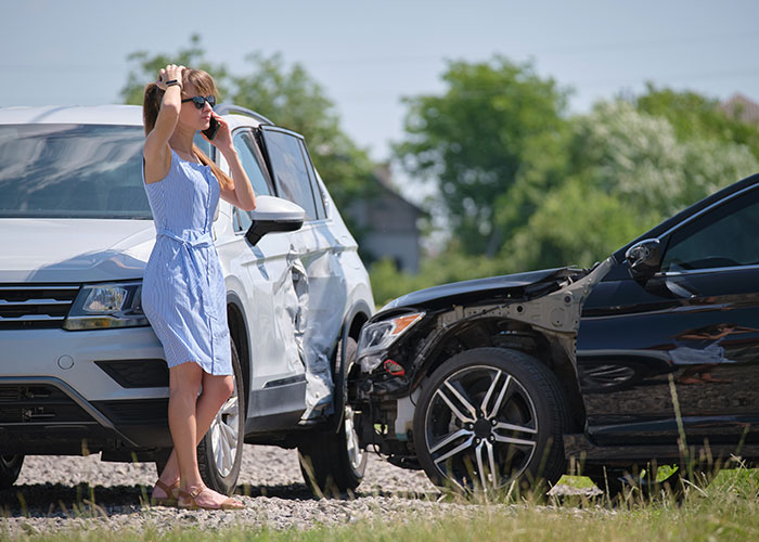 Woman in blue dress making phone call beside damaged cars after accident, reflecting upset feelings in a car crash scenario. Woman in blue dress making phone call beside damaged cars after accident, reflecting upset feelings in a car crash scenario.